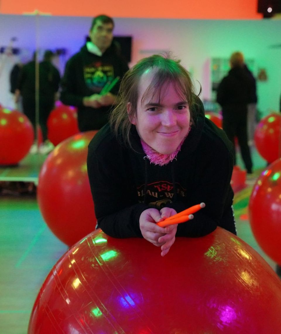 Lachende Trommlerin stützt sich auf ihren roten Ball